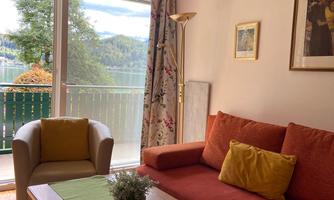 A cozy living room with an orange sofa and a green table runner. Large windows offer a view of the landscape in the background.