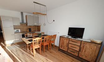 A modern kitchen with a wooden dining table and chairs. The room contains appliances and a television.