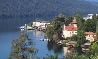 A picturesque lake with gentle hills in the background. Pretty houses and trees stand by the shore.