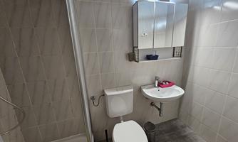 A modern bathroom with a shower, sink, and toilet. The walls are brightly tiled and there is a backlit mirror.