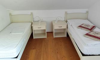 A simple bedroom with two single beds and nightstands. The floor is made of wood and the walls are painted white.