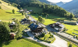 An idyllic alpine landscape with green meadows and charming cabins. In the background, gentle mountains rise under a clear sky.