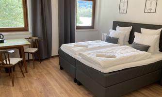 A cozy room with a large bed and big windows. There is a small table with chairs and modern art on the walls.