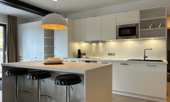 A modern kitchen with a bright color scheme and a central island. The bar stools are black, and a striking lamp hangs over the island.
