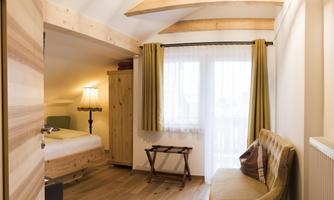 A cozy room with wooden beams and a pleasant ambiance. The room has a bed, a chair, and large windows with curtains.