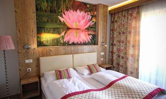 A cozy bedroom with a double bed and a blooming water lily as a mural. The room features light wooden surfaces and floral curtains.