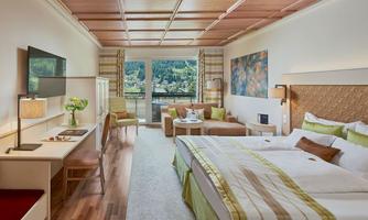 A modern hotel room with two beds, an elegant desk, and a cozy seating area. Large windows offer a view of the landscape.