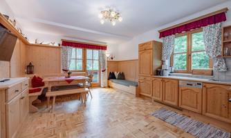 A cozy kitchen with wooden furniture and large windows. The room has a friendly atmosphere and plenty of space for eating and relaxing.