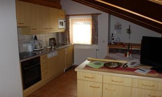 A modern kitchen with wooden cabinets, a stove, and modern appliances. The room is bright and friendly with a window and a small table.