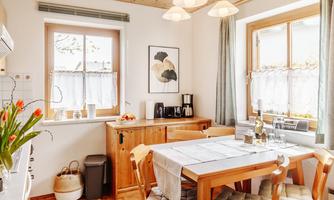 A bright and inviting dining room with a wooden table and chairs. The room features large windows and fresh flowers on the table.