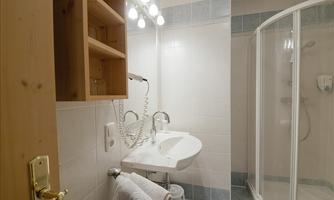 A modern bathroom with a shower, sink, and wooden shelf. The walls are tiled in light colors.