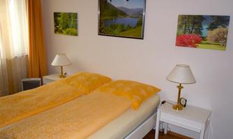 A cozy bedroom with two single beds and yellow bedding. Pictures of landscapes hang on the walls.