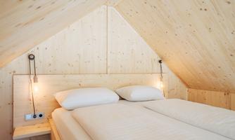 A cozy bedroom in the attic with wood paneling. The bed is equipped with white bedding and modern lamps.