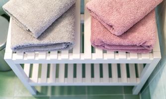 Fluffy towels in gray and pink are laid out on a white shelf. The floor is tiled in green.