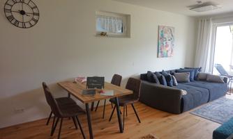A modern living room with a cozy sofa and a wooden table. Large windows provide plenty of light and an inviting atmosphere.