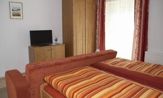 A comfortable room with two beds and a red sofa. There is a television and a large wooden wardrobe.