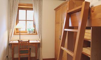 A cozy room with a loft bed, a desk, and a window. The ambiance is warm and inviting, with wooden details and soft curtains.