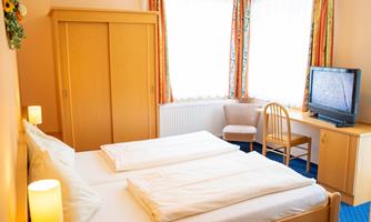 A cozy room with two single beds, a television, and a large window. The room is bright and cheerfully furnished.