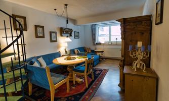 A cozy living room with blue sofas and a round table. There is a staircase, a wooden dresser, and a rug that makes the room warm and inviting.