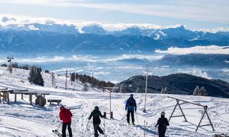 A snowy mountain landscape with skiers. In the background, impressive mountains and a clear sky can be seen.