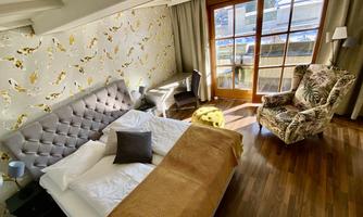A cozy bedroom with a large bed and a comfortable armchair. Large windows provide plenty of daylight and a view outside.