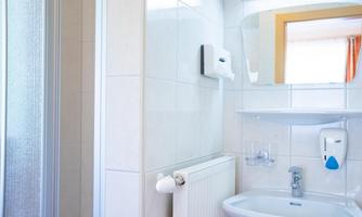 A modern bathroom with a shower, a sink, and a large mirror. The walls are brightly tiled, and there are windows with curtains.