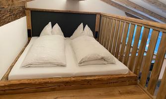 A cozy bedroom with a large bed and white pillows. The wooden ceiling and walls give the room a warm, rustic character.