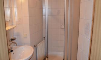 A small bathroom with a shower, a sink, and a toilet. The walls are covered with white tiles.