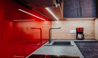 A modern kitchen with glossy red walls and elegant black surfaces. The amenities include a stove, a modern faucet, and a coffee machine.