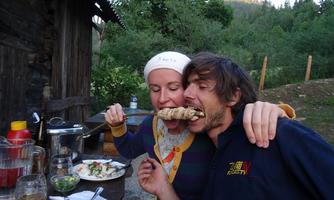 A couple is sitting outdoors and enjoying a shared meal. They are sharing a large skewer and having fun together.