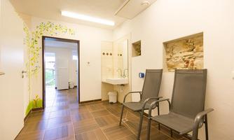 A modern room with two chairs, a sink, and a wall with a decorative pattern. There is a view of an outdoor area through a door.