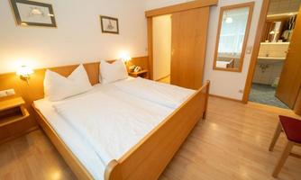 A cozy bedroom with a double bed and wooden interior. The room is bright and has a mirror as well as access to a bathroom.