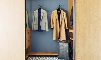 A well-organized wardrobe with two jackets, a suitcase, and a blue wall. The wooden shelves give the room a modern look.
