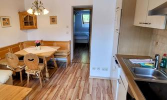 A bright and inviting kitchen with a dining table and wooden paneling. In the background, a bedroom is visible.