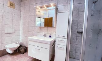 A modern bathroom with bright tiles and a sink under a large mirror. There is a shower and a toilet in the corner.