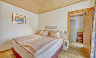 A cozy bedroom with a large bed and two pillows. The warm wooden tones create an inviting atmosphere.
