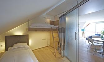 A cozy bedroom with a single bed and a loft bed. The modern decor and the bright wooden floor create an inviting atmosphere.