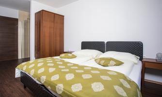 A cozy bedroom with a double bed and a green duvet. In the background, there is a wardrobe and there is a small table next to the bed.