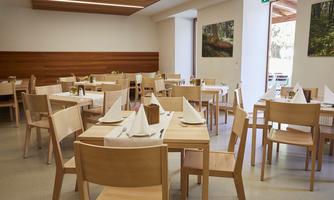 A bright restaurant area with wooden tables and chairs. The tables are set with white napkins and decorative elements.