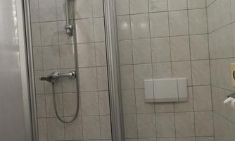 A small bathroom with a shower and a toilet. The walls are tiled and the furnishings are simple and functional.