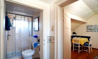 A bathroom with a shower and toilet that overlooks a living area. The dining area is bright and cheerfully furnished.