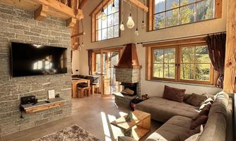 A cozy living room with high ceilings and wooden beams. Large windows let in plenty of daylight and offer a beautiful view.