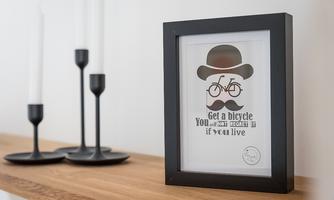 A framed picture featuring a bicycle and a stylized mustache. The text reads: "Get a bike, you won't regret it when you live."