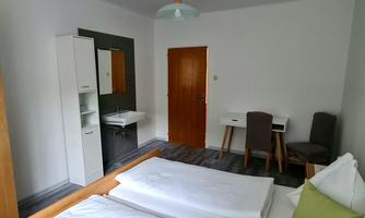 A simple room with two beds, a table and a chair. There is a sink and a wardrobe on the wall.