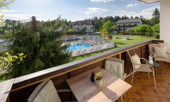 A cozy terrace overlooking a swimming pool and well-kept gardens. The surroundings are green and inviting.