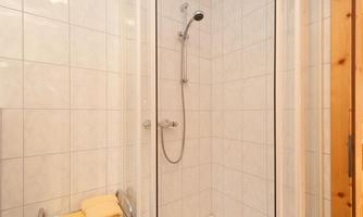 A modern shower with white tiles and a clear shower partition. Yellow towels are neatly arranged on a rack.