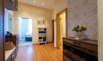 A bright entrance area with wooden flooring and a decorative sideboard. In the background, a bedroom and a bathroom are visible.