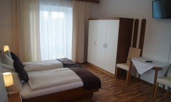 A cozy room with two single beds, bright curtains, and a television. The floor is wooden, and a table with chairs is also present.