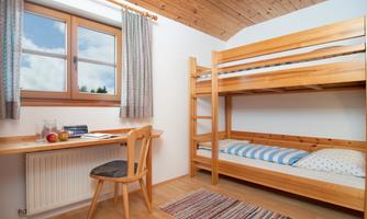 A simple room with a bunk bed and a desk. Large windows allow for plenty of daylight.