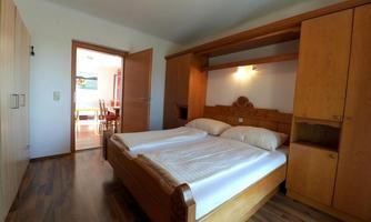 A cozy bedroom with a double bed and wooden furniture. The room is bright and offers a view of an adjacent dining area.